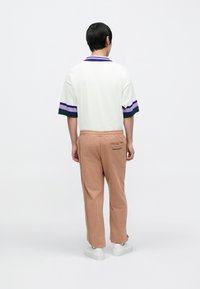 Valkoinen, teksturoitu lyhythihainen poolopaita, jossa violetteja ja vihreitä raitoja; beiget collegehousut, joissa on sivutasku ja takaosassa teksti "CARD COLLECT".