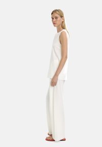 Biała bezrękawnik zestawiona z szerokimi białymi spodniami. Gładki materiał o minimalistycznym wzorze. Podkreślona jaskrawymi pomarańczowymi klapkami.