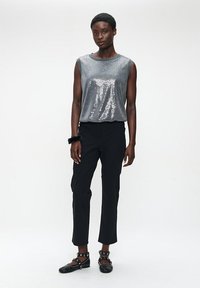 Silberne Pailletten-Ärmellose Bluse mit rundem Ausschnitt, kombiniert mit schwarzen Slim-Fit-Hosen und besetzten schwarzen Ballerinas. Akzentuierter schwarzer Armreif.