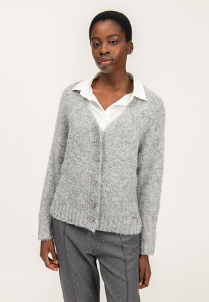Cárdigan gris con textura, con cuello en V, mangas largas y cinco botones. Combinado con una camisa blanca con cuello y pantalones grises con lunares.