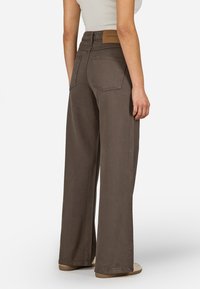 Široke rjave hlače iz bombaža. Imajo dva zadnja žepa in usnjeno stvar za pas. Gladko teksturo in sproščen dizajn.
