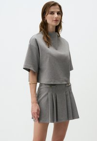Grauer Cropped-Top mit kurzen Ärmeln und hohem Kragen, kombiniert mit einem plissee Minirock. Beide Teile haben dünne vertikale Streifen in Hellgrau.