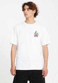 T-shirt en coton blanc à manches courtes, avec un graphique coloré d'un chat dans une télévision sur le côté gauche de la poitrine. Coupe décontractée et col rond.