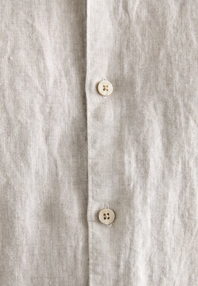 Lichtbeige linnen shirt met een knoopsluiting aan de voorkant, voorzien van twee ronde, lichte knopen en een gestructureerde stofoppervlak.
