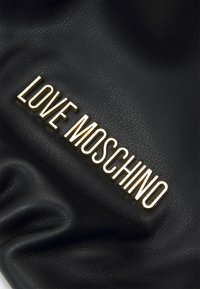 Svart texturerat läder med en guldtonad "LOVE MOSCHINO"-logotyp som är tydligt synlig. Materialet har en mjuk, rynkad yta.
