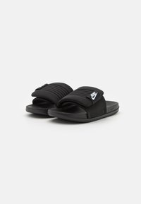 Black slide sandals with a textured upper, featuring a wide strap and a logo accent. Soft material and flat sole for comfort.