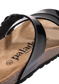Sandale en cuir verni noir avec deux larges brides, semelle en liège et semelle en caoutchouc. Présente la marque "palado" sur la semelle.