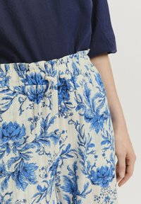 Weiße Hose mit blauem Blumenmuster, elastischem Taillenbund mit Kordelzug, ausgestattet mit vertikalen strukturierten Streifen. Dazu ein marineblaues Oberteil.