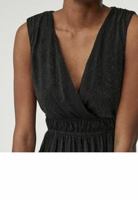 Musta mekko, jossa on syvä V-mallinen kaula-aukko ja hihaton muotoilu. Siinä on kokoontuva elastinen vyötärö ja teksturoitu kangas, jossa on hienovarainen kiilto.