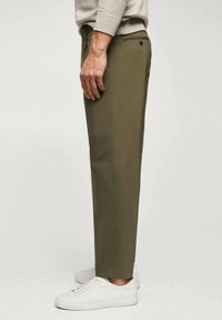 Pantaloni verde oliva realizzati in tessuto intrecciato, dal taglio dritto, con chiusura a bottone, tasche laterali e indossati con sneakers bianche.