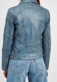 Giacca di pelle blu con una finitura testurizzata, caratterizzata da un design strutturato, cuciture visibili e polsini con zip. Parte di un outfit in denim.