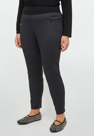 Wąskie ciemnoszare spodnie z przednimi kieszeniami na suwak, noszone z czarnymi balerinami z ćwiekami i czarną bluzką z długim rękawem.