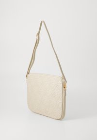 Sac à main matelassé beige avec motif de roses, texture lisse et bandoulière ajustable. Il dispose de ferrures dorées et d'une fermeture éclair.