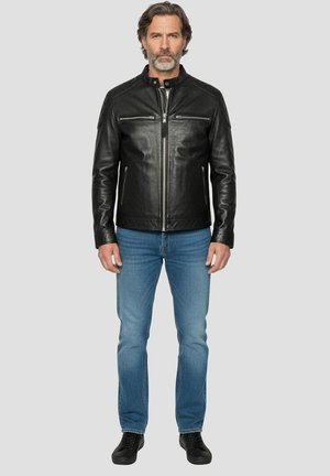 Sort lædermotorcykeljakke med lynlås, to brystlommer og en opretstående krave. Kombineret med blå jeans og sorte sko.