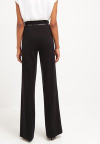 Zwarte wijde broek met hoge taille, voorzien van een gestructureerde riem met studs, gladde stof en een nauwsluitende pasvorm.