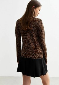 Pull en imprimé léopard marron avec des manches longues, ourlet côtelé ; associé à une jupe plissée noire. Texture lisse, design ajusté.