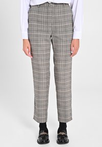 Graue karierte Hose mit maßgeschneidertem Schnitt, aus strukturiertem Stoff und mit Knopfverschluss. Kombiniert mit schwarzen Mokassins und Socken.
