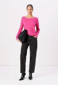 Rosa långärmad topp, svarta högmidjade raka jeans och svarta spetsiga klackar. Modell som håller en svart clutchväska. Slät textur.