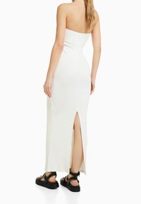 Witte geribbelde midi-jurk met een aansluitend ontwerp en een zijsplit. Gecombineerd met zwarte sandalen met studs voor contrast.