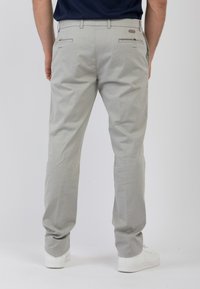 Chinos grigio chiaro con una texture liscia e un design a gamba dritta. Presenta tasche posteriori con piccole alette e un dettaglio del logo sopra la tasca destra.