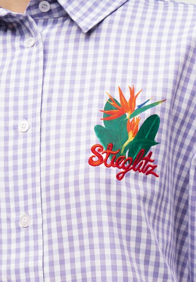 Λιλά και λευκό καρό πουκάμισο με πολύχρωμο κεντητό λουλούδι παραδείσου και κόκκινα γράμματα "Stieglitz" στο στήθος.