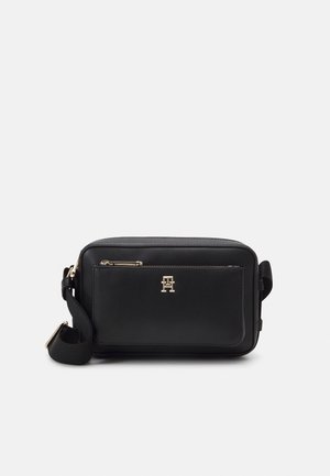 Sac bandoulière rectangulaire noir avec logo doré et fermeture éclair, sangle ajustable et poche avant, présenté sur fond blanc.