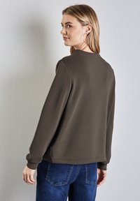 Felpa marrone con scollatura rotonda e maniche lunghe, abbinata a jeans in denim. Tessuto liscio e design semplice, senza motivi visibili.