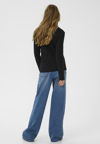 Zwarte gebreide trui met een ribbelstructuur, gecombineerd met wijde blauwe denim jeans. De outfit heeft een eenvoudig, minimalistisch ontwerp.