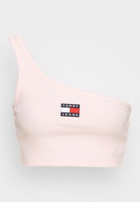 Jednobarevný světle růžový crop top s jedním ramínkem vyrobený z ribbed látky. Na přední straně se nachází černá a barevná nášivka s logem "TOMMY JEANS".