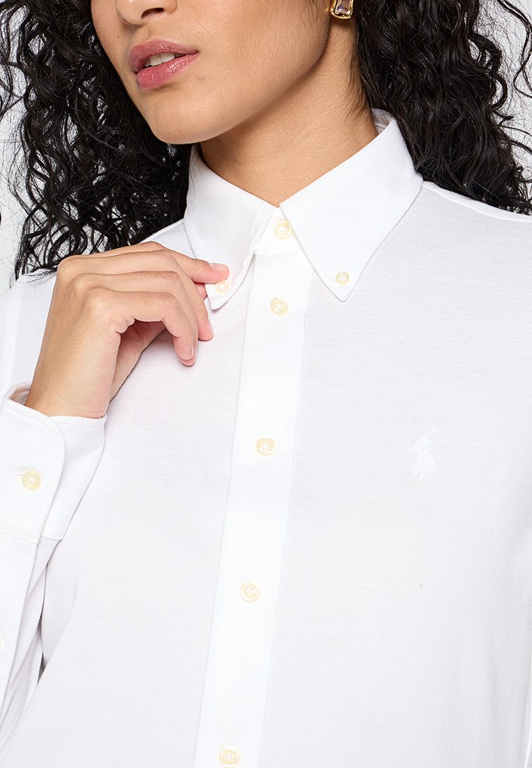 Camicia bianca con bottoni, realizzata in un tessuto strutturato, con bottoni gialli e un piccolo logo ricamato sul petto. Design con colletto.