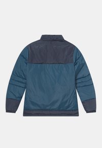 Gewatteerde jas gemaakt van een mix van donkerblauwe en marineblauwe materialen. Kenmerkt zich door een staande kraag en elastische manchetten, met een gestructureerde, gladde afwerking.