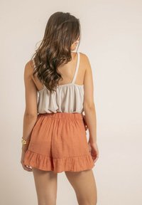 Haut gris clair élastique avec des bretelles spaghetti associé à un short froncé corail-orange. Tissu doux et texturé avec une coupe décontractée.