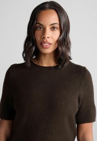 Brauner, kurzärmeliger Pullover mit geripptem Muster und rundem Ausschnitt, der dezente Schulternähte und eine glatte Oberfläche aufweist.