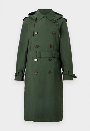 Trenci verde cu nasturi dubli, curea în talie și glugă. Dispune de mansete prevăzute cu nasturi și o textură subtilă.