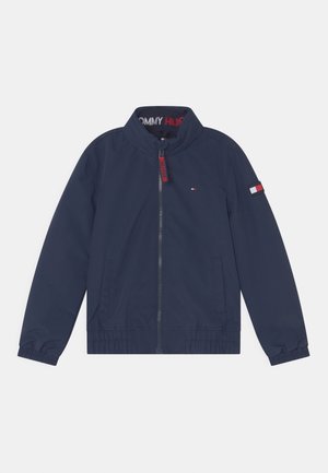 Marineblå jakke med lynlås og stående krave, elastiske manchetter, frontlommer og lille Tommy Hilfiger-logo på brystet og venstre ærme.