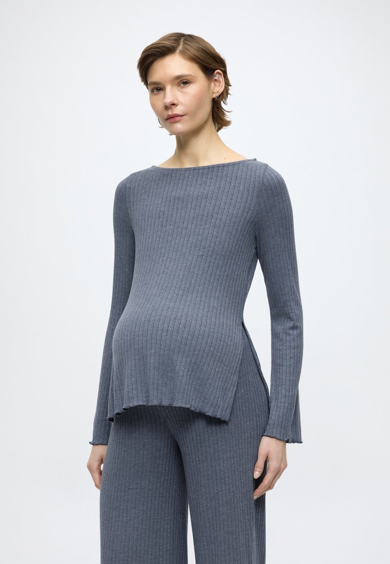 Γκρι ριμπ τοπ εγκυμοσύνης με μακριά μανίκια και πλευρικές σχισμές, με λαιμόκοψη τύπου βάρκα. Ομαλή υφή, σε συνδυασμό με ταιριαστό ριμπ παντελόνι.