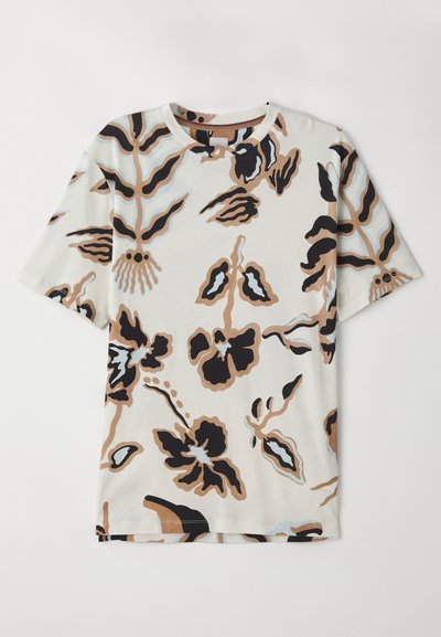 Kortærmet T-shirt lavet af blødt stof, med en cremefarvet baggrund og abstrakte blomster mønstre i sort, brun og lyseblå.