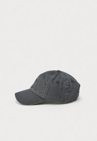 Boné de beisebol preto desgastado em algodão lavado, com aba curva e ilhós de ventilação costurados, sobre um fundo branco.