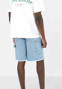 Shorts in denim blu con orlo sfilacciato, dotati di tasche posteriori e un fit rilassato, abbinati a una T-shirt bianca con grafica.