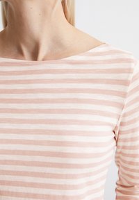Striped long-sleeve top in soft pink and white. Features a boat neckline and a lightweight, textured fabric. Visible seam detailing.