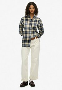 Chemise en flanelle à boutons en crème et motif à carreaux bleu marine ; coupe décontractée. Assortie à un pantalon large en crème et des mocassins bruns.