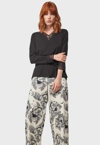 Haut noir à manches longues avec des accents en dentelle et un col en V, associé à un pantalon large blanc avec un imprimé floral noir et des hiboux.