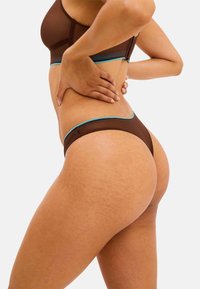 Bra aus transparenter brauner Spitze und passendem Tanga mit türkisfarbenen, gewellten Akzenten, die eine glatte Stofftextur und eine taillierte Form zeigen.