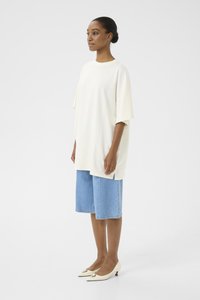 Crème oversized t-shirt, blauwe denim shorts en beige kitten heels. T-shirt heeft een ronde halslijn en een losse pasvorm. Minimalistische stijl.