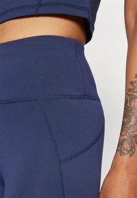 Tengerészkék sport leggings sima, rugalmas textúrával, ívelt varrásokkal és elasztikus derékkal, a kényelem és a rugalmasság érdekében tervezve.