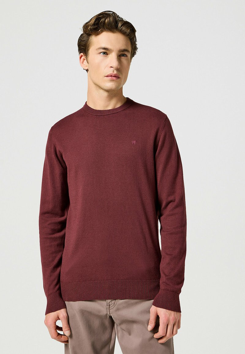 Maglione bordeaux a maniche lunghe in morbido materiale a maglia, con scollatura rotonda e polsini a costine. Piccolo logo sul petto.