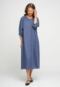 Abito in lino blu con bottoni frontali, maniche a tre quarti e scollatura arricciata. Di lunghezza media, presenta una vestibilità morbida e una texture delicata.