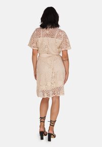 Koronkowa sukienka midi w odcieniu nude, z krótkimi falbankami, talią podkreśloną paskiem i falbaniastym dołem. Zestawiona z czarnymi sandałami na słupku z paskami.