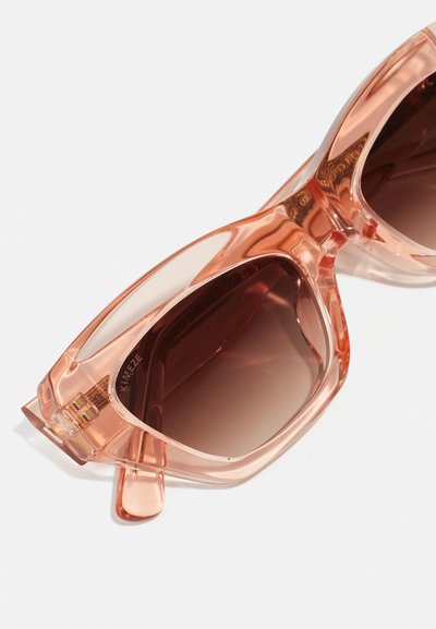 Rosa transparenta solglasögon med bruna gradientlinser. Kraftig rektangulär ram, slät yta och diskret logotyp på insidan.