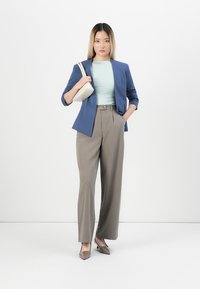 Modrý blejzr přes světle tyrkysový top, doplněný šedými kalhotami s vysokým pasem. Bílá kabelka a béžové podpatky dotvářejí outfit.